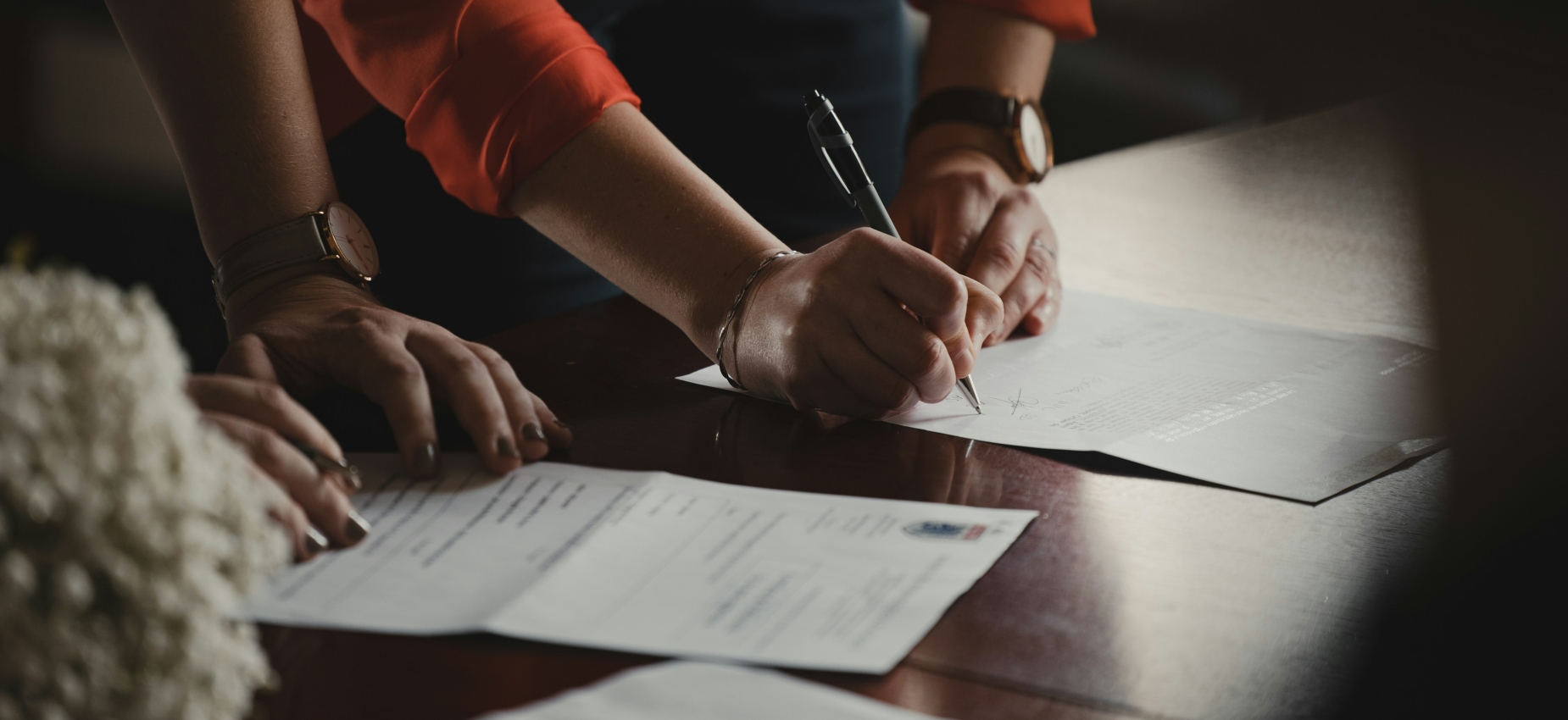 Hands signing a transaction agreement at a meeting table