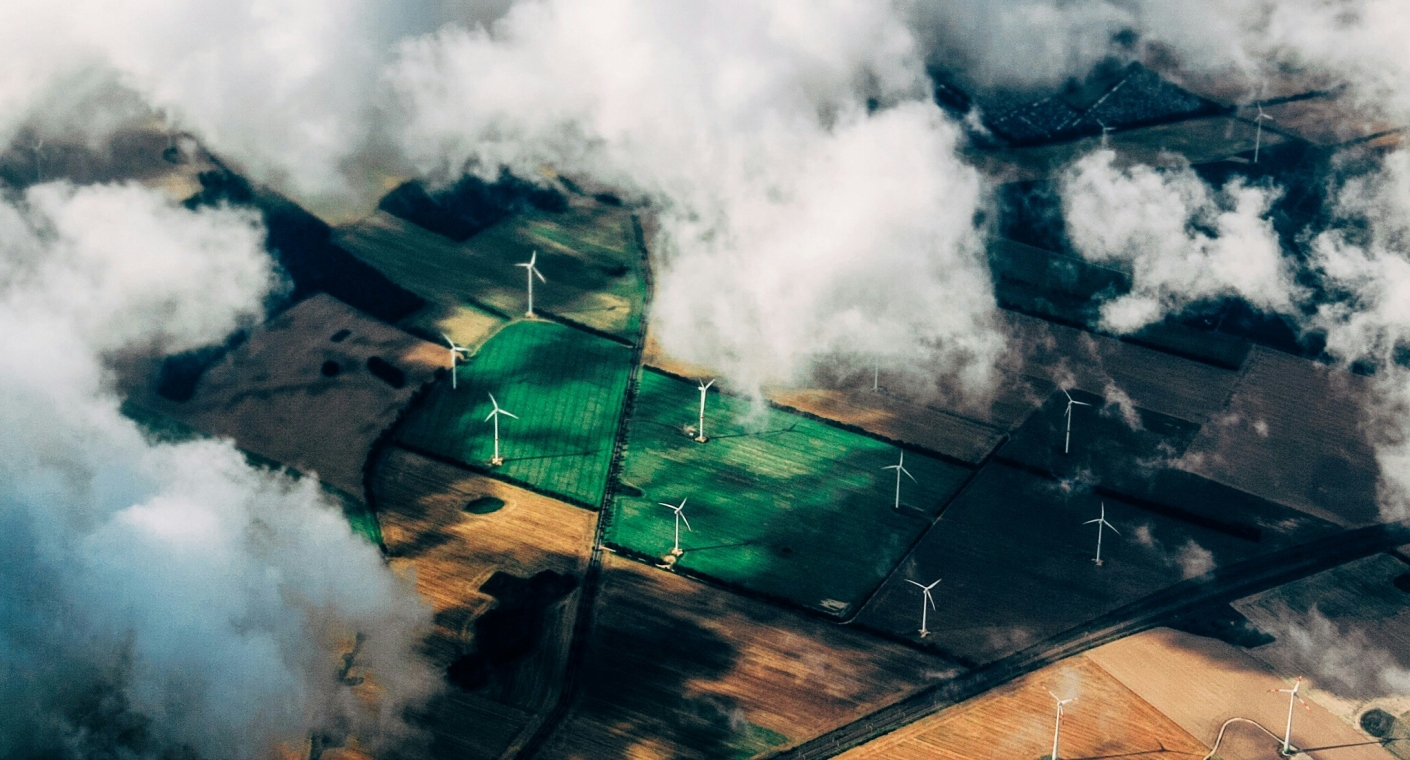 Aerial view through the clouds of onshore wind turbines in green farmland