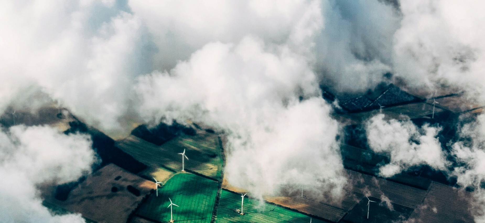 Aerial view through the clouds of onshore wind turbines in green farmland